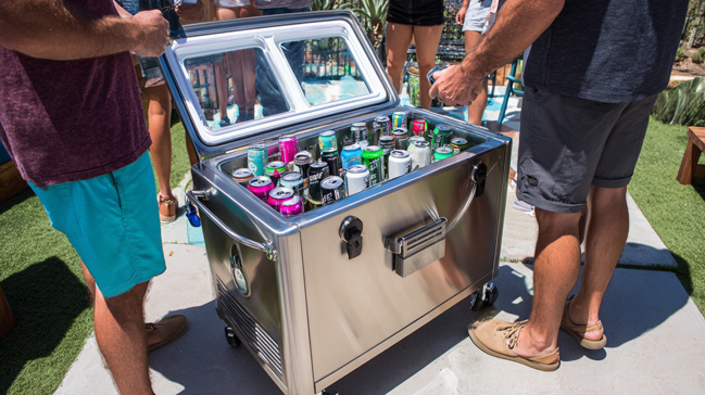 Stylish rolling cooler with built-in bottle opener serving as outdoor beverage station during BBQ party